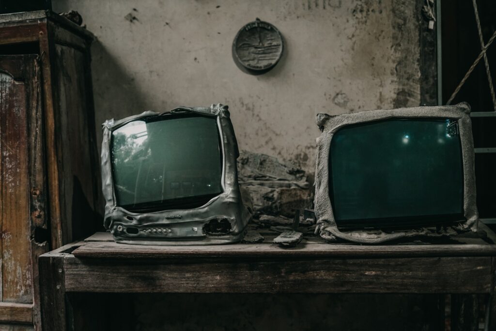 two old televisions on a desk next to a cupboard